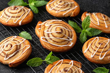 Freshly baked sweet cinnamon swirls with icing on cooling rack. Sweet food