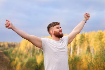 young bearded relaxed calm man enjoying good weather in the forest, park, breathing deep fresh air and smiling. Guy with beard holding his arms hands up behind head, stratching with his eyes closed