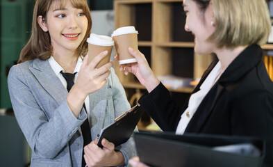 Business women clinking cups of coffee in office.
