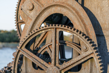 Close up on a rusty mechanism at the edge of a river. Different gears are visible.