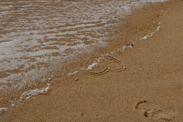 Close up on the foam of a wave occulting a love heart hand drawn in the sand of a beach.