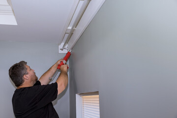 Construction worker syringe fills seam between cornice and wall with acrylic latex caulk silicone sealant © ungvar
