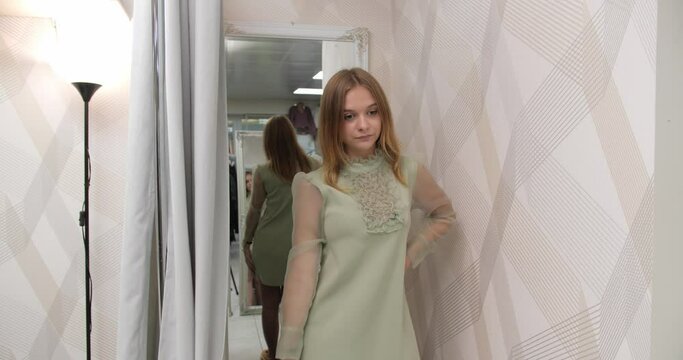 The girl leaves the fitting room in the store and looks at herself in the mirror