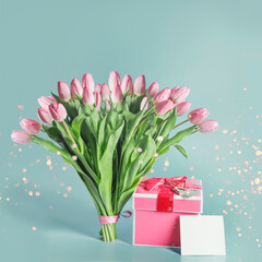 Beautiful pink tulips bunch with gift box, greeting card mock up and bokeh at blue background.