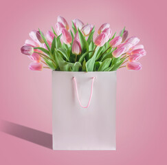 Bunch of beautiful tulips bunch in paper shopping bag at pink background. Greeting and holiday concept