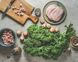 Green kale leaves on kitchen table with ingredients for tasty cooking: smoked pork meat, mushrooms, herbs and spices, top view.