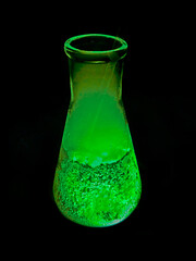Glass containing reactive mysterious green liquid on black background