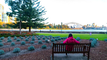 Fototapeta premium beautiful girl siting on the bench with famous sydney opera house in background; sunrise over sydney opera house, sydney walk at sunrise