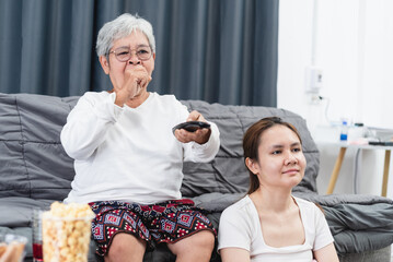 Asian senior woman presses the TV remote, she is yawning and her daughter is sleepy, the TV show is too boring.