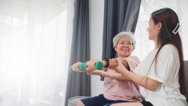 Asian Woman Helping Her Mother Senior Woman, Lifting Dumbbells And Exercising At Home.