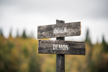 vintage and rustic wooden signpost with the weathered text quote inner demon, outdoors in nature. blurred out forest fall colors in the background.
