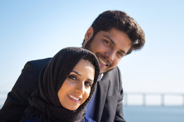 Close-up of young lovely Muslim couple standing close. Happy smiling bearded man and nice woman posing on blue sky and sea background. Vacation, romance and dating concept