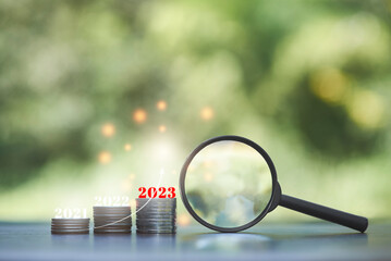 magnifying glass and rows of coins on the table and 2023 ,business goals, savings, business growth, investments concept