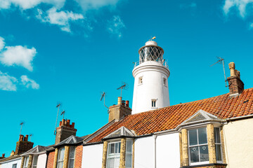 Coastal lighthouse seen rising above the roofs of terraced houses against a summer sky at a popular Suffolk coastal town.