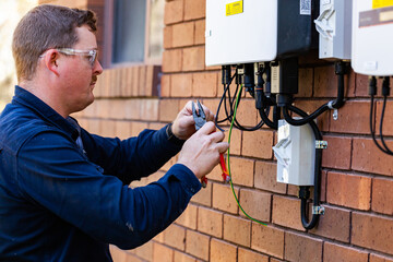Tradie working as an electrician wiring a solar power control box beside house