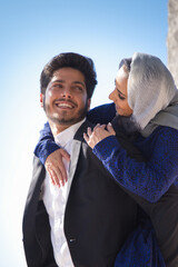 Portrait of young loving Arabian couple hugging. Beautiful woman in headscarf hugging happy man neck from his back and they tenderly looking at each other. Happiness, relationship and romance concept