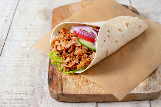 doner donair kebab wrap with spicy meat, lettuce, tomato, red onion. Served on wooden cutting board. Copy space for text or logos.