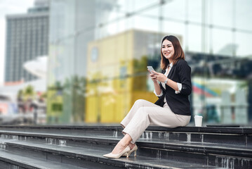 Young Asian businesswoman using tablet and walking in airport before business trip. Beautiful woman passenger has mobile call and discusses something with smile, holds coffee in hand