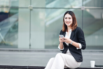 Young Asian businesswoman using tablet and walking in airport before business trip. Beautiful woman passenger has a mobile call and discusses something with smile, holding coffee in hand