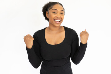 Portrait of happy young woman making winning gesture against white background. African American...