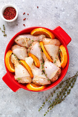 Raw Chicken Drumsticks with Oranges and Thyme, prepared for baking in red round baking dish