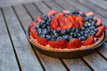 Fresh homemade beautiful fruit tart with blueberries and sliced ​​strawberries on top on a wooden table