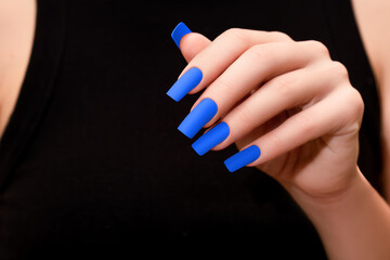 Female hands with blue nail design. Mate blue nail polish manicure. Female model in black dress...