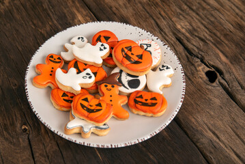 Bright orange cookies for Halloween in the shape of pumpkin ghosts in plate on a wooden table. Top view.