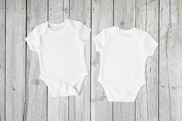 Two white baby bodysuits mockup, front and back view of baby onesie for design presentation, top view on wooden background.