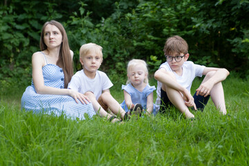 Woman with three children resting on grass in park. Young mother with daughter and sons sits on green lawn