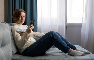 Beautiful smiling girl relaxing on a couch and using mobile phone
