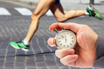 measuring the running speed of an athlete using a mechanical stopwatch. hand with a stopwatch on the background of the legs of a runner.