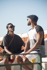 Portrait of two happy African gay men staring at each other. Romantic couple in casual clothes sitting close on bench on roof top and both lovers looking serious. Same sex love, relationships concept