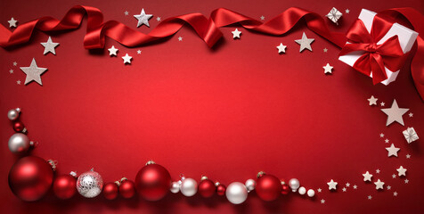 Christmas background in red, with a border composed of baubles, gift box, stars and ribbon, framing free wide format copy space