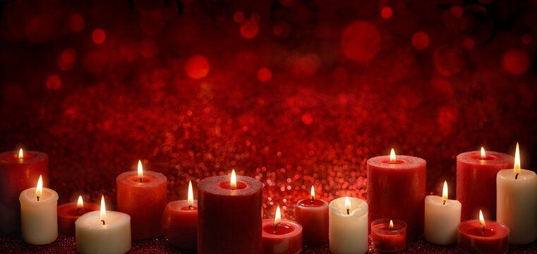Burning candles as a border on a red festive background with glittering bokeh lights, ideal for Christmas or religious events, wide format with copy-space