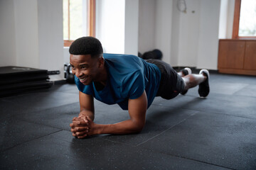 Happy young black man in sportswear doing plank exercises at the gym