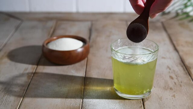 matcha Collagen powder is add to glass of water with a spoon. Healthy and anti-age concept