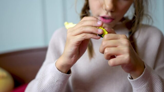 Kid Girl Is Engaged In Weaving From Yellow Rubber Bands At Home