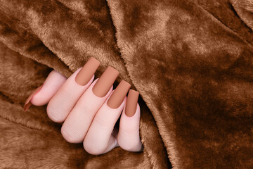 Female hand with brown nail design. Mate brown nail polish manicure. Female model hand on brown...