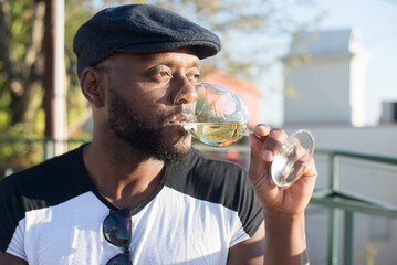 Close-up of young African American man enjoying wine. Happy brown-eyed man in casual clothes...