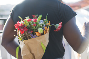 Back view of African man bringing flowers for date. Sporty man holding bouquet of beautiful flowers behind his back waiting and looking straight. Dating, relations, romance and love concept