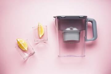 Water filter jug and glass of water with lemon on a pink background. Top view.