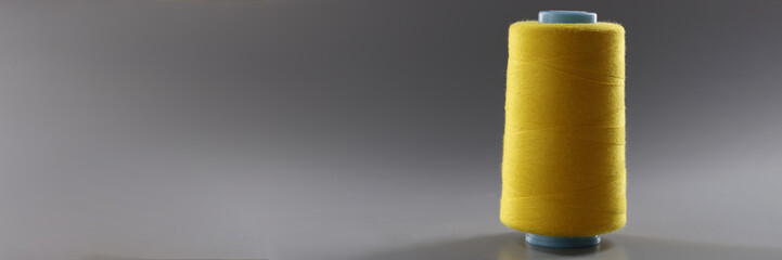 Big yellow bobbin of thin threads on a gray background