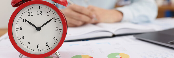Red alarm clock on documents in the office, woman is blurry
