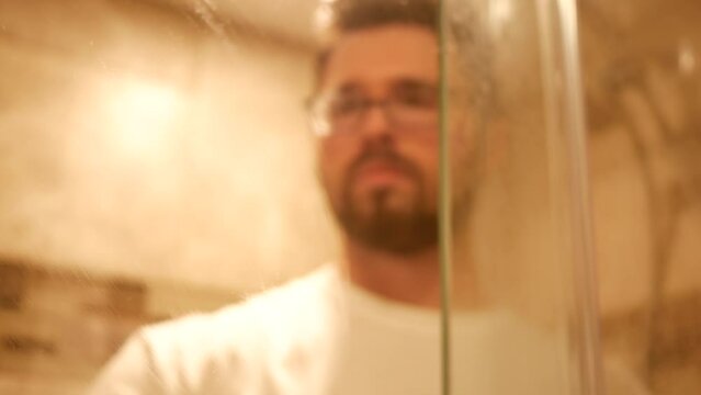 Man cleans the inside of shower class door in modern tile shower