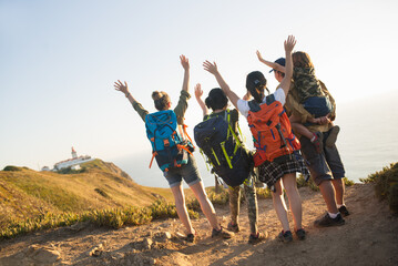 Rear view of happy backpackers raising arms on mountain. Family hiking together in summer. Active family concept