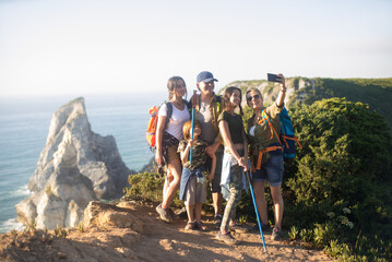 Happy family of backpackers posing for selfie at precipice. Parents with daughters and son hiking in mountains in summer. Active family weekend concept