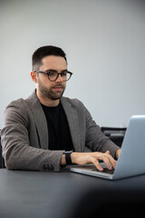 caucasian man sitting in front of laptop typing, man with glasses sitting in front of a computer