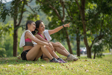 Two young women sitting at the park and relaxing after jogging outdoors.