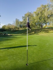 Golf Course green with blue sky and flag in view, autumn day with dew